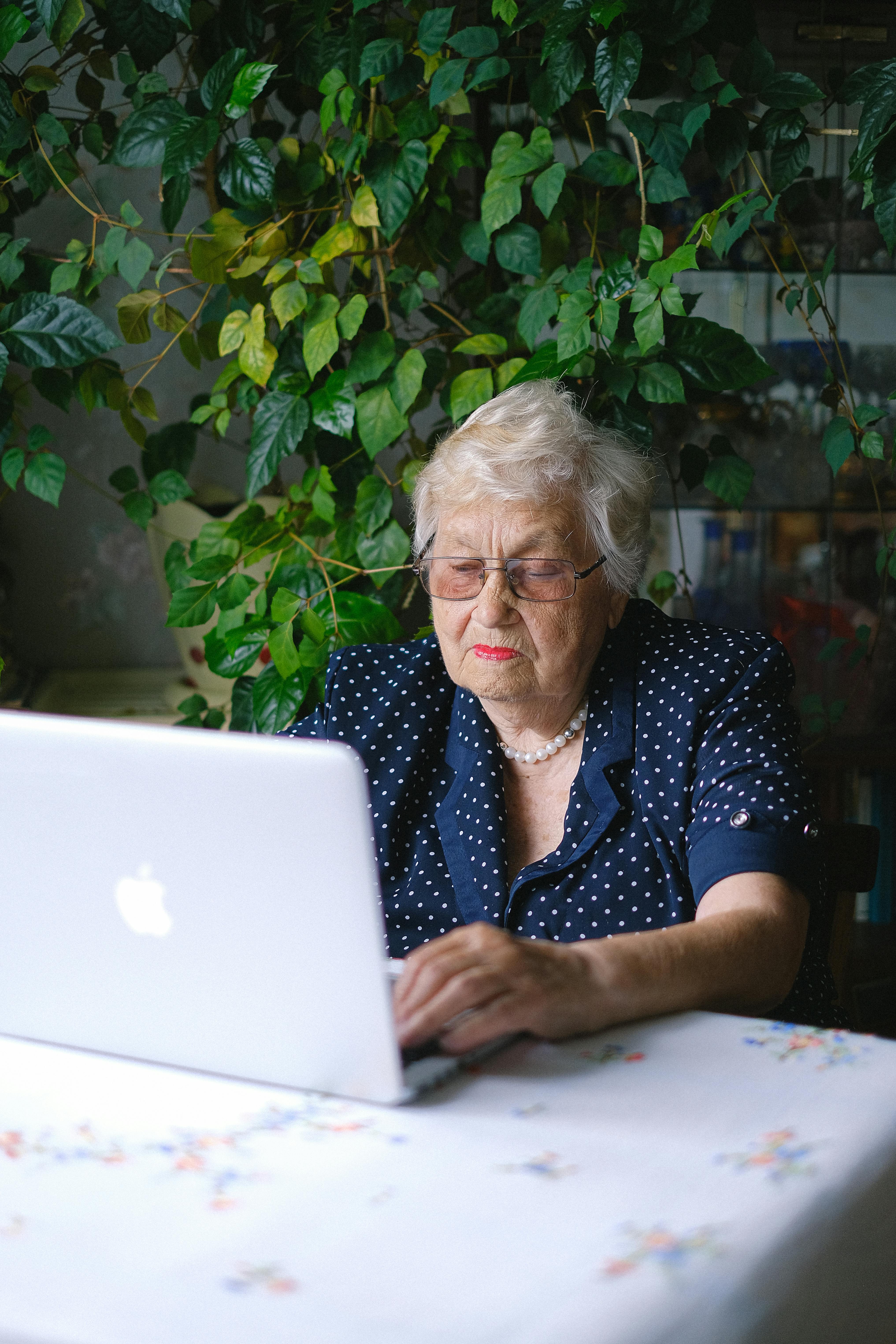 Senior woman working on a laptop surrounded by indoor plants.