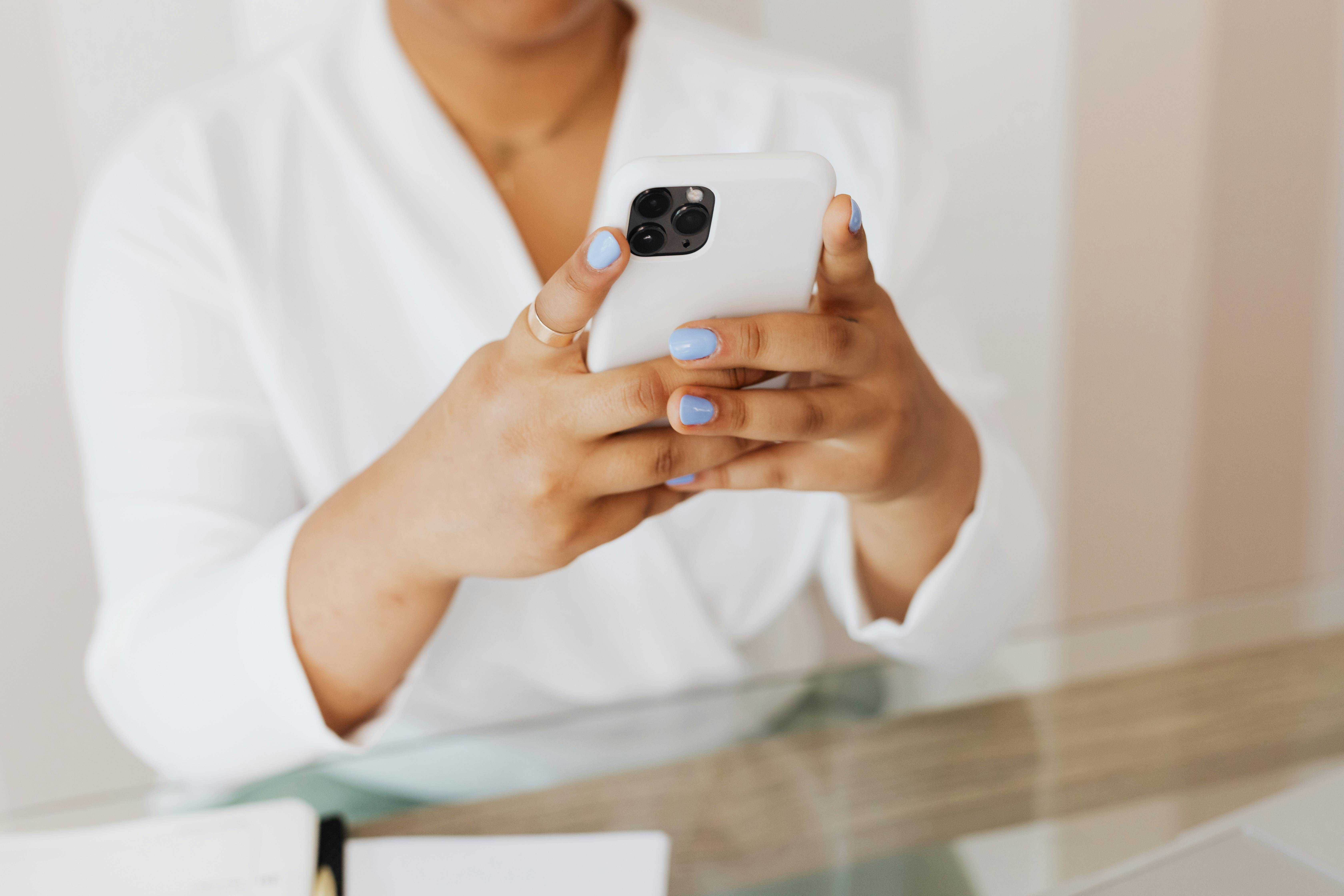 Close-up of a person holding a smartphone indoors with a focus on manicured nails.